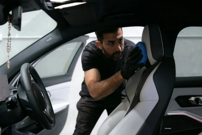 A man cleans a car seat inside the vehicle.